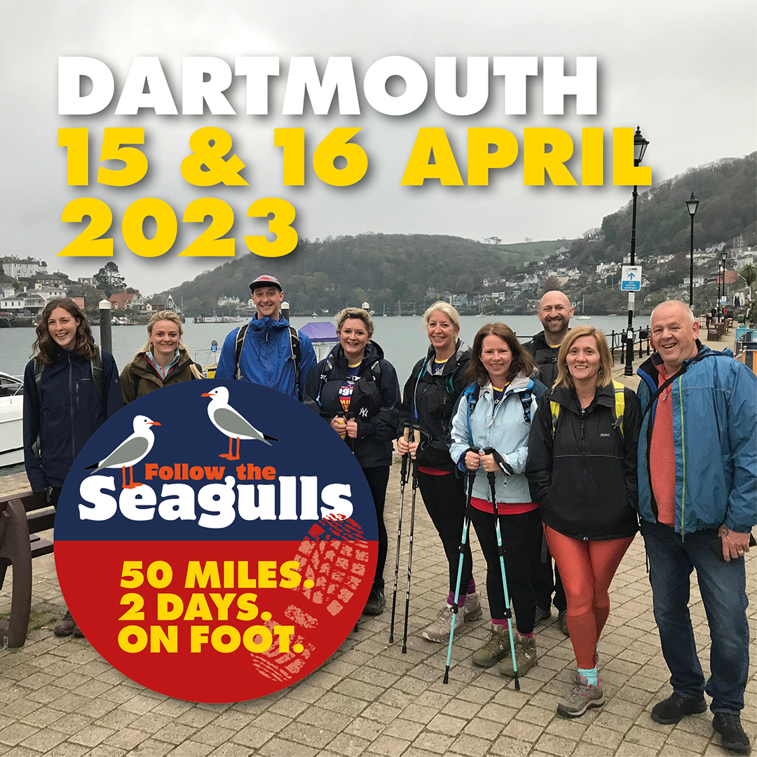 Text reads: Dartmouth. 15 and 16 April. ID: group of charity walks stood in walking gear in front of harbour with cliffs in background.