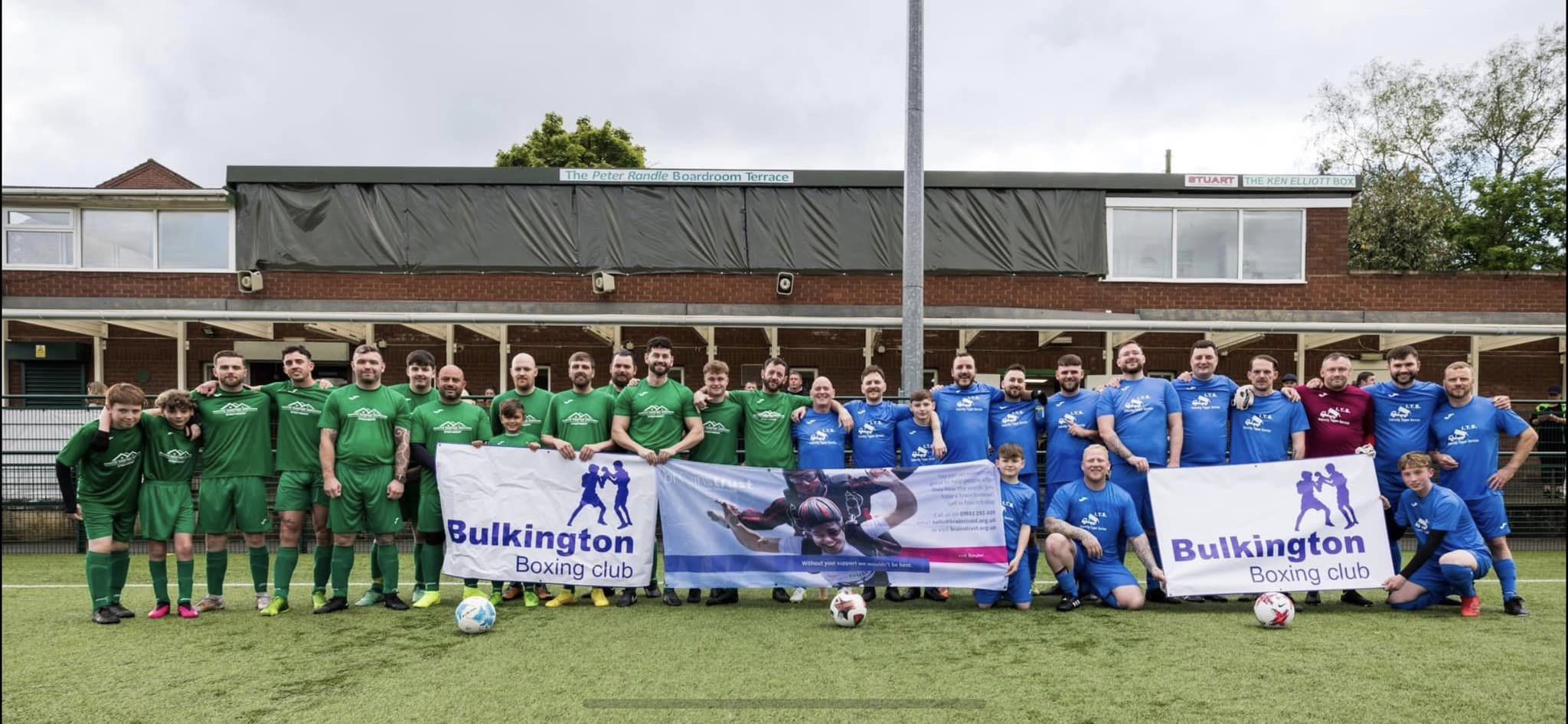 Image shows two football teams arm in arm on football pitch holding up a brainstrust poster. 
Image from Cheryl's charity football match for brainstrust